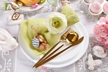 Easter tableware with golden cutlery and green napkin on white plate