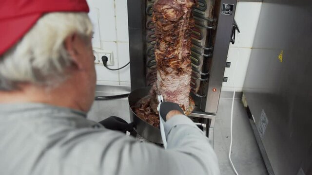 Close up view of fast food worker cutting the meat for doner kebab meal off rotating meat stick in traditional Middle Eastern dish