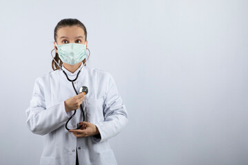 Woman doctor in white uniform wearing a medical mask and holding stethoscope