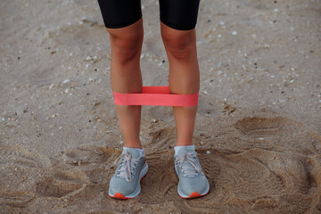 beautiful sports girl is engaged in fitness with rubber bands by the sea