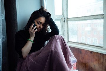 a depressed girl sits at the window and talking on the phone