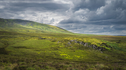 Green hills and fields illuminated by sunlight in Cuilcagh Mountain Park with dramatic stormy sky, Northern Ireland