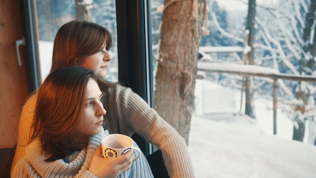 Two fashionable beautiful lesbian girls are sitting near the window and drinking coffee. High quality photo