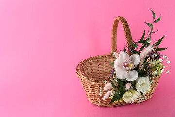 Fototapeta na wymiar Wicker basket decorated with beautiful flowers on pink background, space for text. Easter item