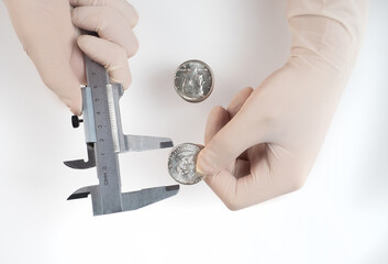 hands in rubber gloves with a caliper measure a silver dollar coin