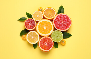 Fresh juicy citrus fruits with green leaves on light yellow background, flat lay