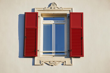 Italian window on the bright white wall facade with open red color classic shutters