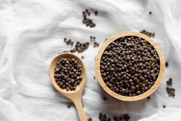 A large number of black peppercorns placed in a wooden bowl were placed on a white cloth.
