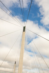 Architecture detail of a Pedestrian bridge support tower and cables against a blue sky with puffy clouds