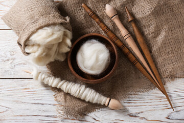 Soft wool and spindles on white wooden table, flat lay