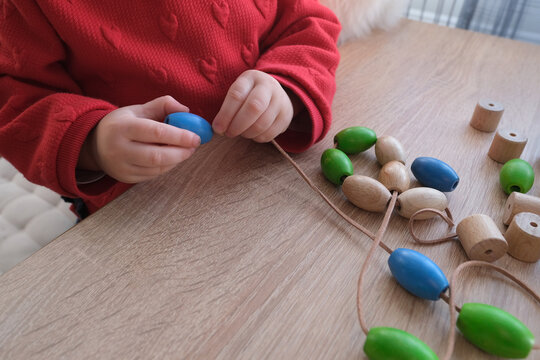 small child, toddler stringing colored wooden beads on a string, children's fingers close-up, concept of development of fine motor skills, tactile sensations, creativity, children's entertainment