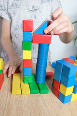 small child, kid plays with colored wooden cubes, builds houses and rockets, the concept of the development of creativity, fine motor skills, patience and perseverance