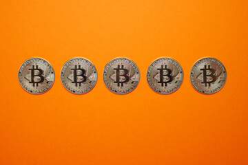 Silver Bitcoin coins in horizontal row on orange background. Cryptocurrency