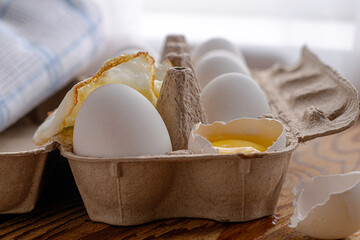 chicken eggs in a cardboard tray one egg is broken the other fried in fried eggs