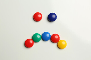 Sad face made with colorful magnets on white background, flat lay