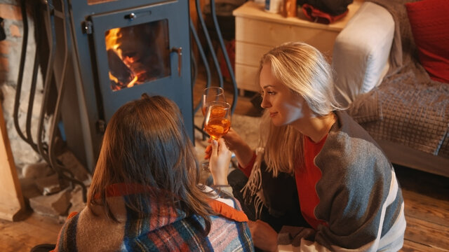 two young women, lesbian couple relaxing near the fireplace and drinking wine in the cozy home. High quality photo - Powered by Adobe