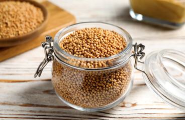 Mustard seeds in glass jar on white wooden table, closeup