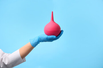 Doctor holding pink enema on light blue background, closeup