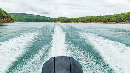 Rear view of a speedboat ride on the lake making waves and the landscape of the Lake of Furnas at...