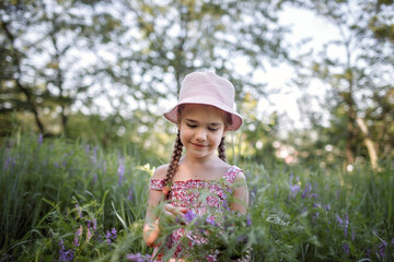 Girl in summer linen dress walking among trees in the forest and gathering wild flowers bouquet, slow living in the village, far from the big city, healthy lifestyle