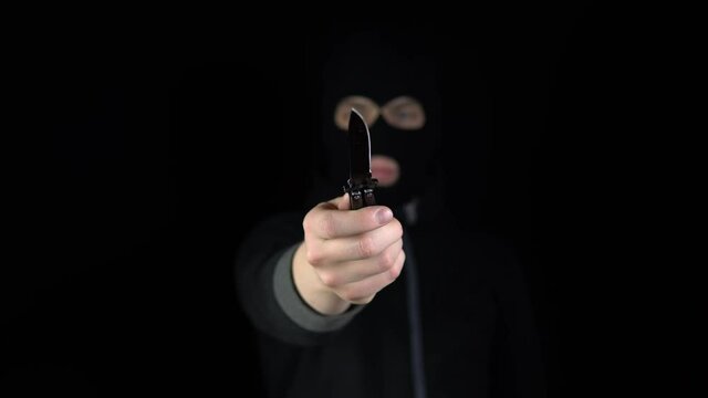 A man in a balaclava mask holds out a butterfly kn