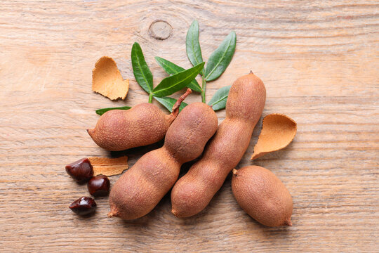 Ripe tamarinds and fresh leaves on wooden table, flat lay