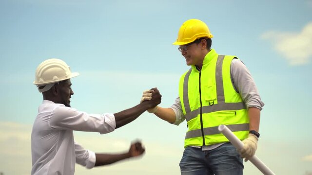 asian foreman and african american architect handshake  outdoors on construction site on blue sky . contractor worker Inspection with builder . Engineer and foreman. quality control . diversity people