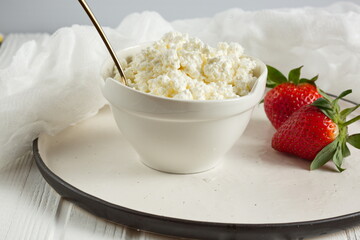 White bowl with fresh red ripe strawberries and natural cottage cheese, on white wooden table for fitness breakfast. Dietary product. The concept of healthy eating.
