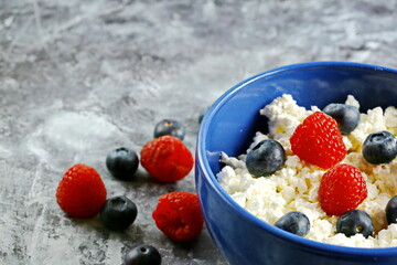 Blue bowl with fresh red ripe strawberries and blueberries and natural cottage cheese, on white wooden table for fitness breakfast. Dietary product. The concept of healthy eating.