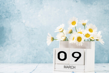 White cube calendar for march decorated with daisy flowers over blue with copy space