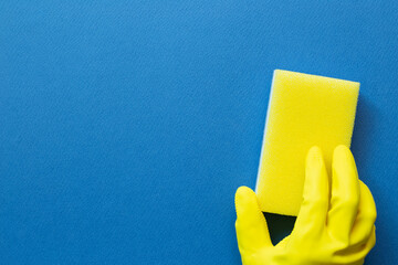 Hand in yellow glove hold sponge on blue background. Cleaning concept. top view, copy space