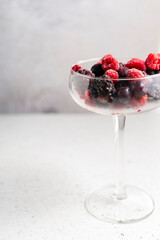 frozen blueberries, raspberries and blackberries on a light textured background. in a tall transparent cocktail glass. copyspace