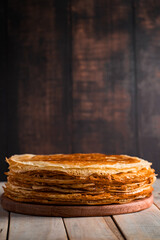 A stack of thin pancakes on a dark wooden background. A traditional dish of crepes for the holiday Maslenitsa.