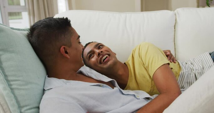 Smiling mixed race gay male couple hugging lying on sofa together