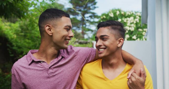 Smiling mixed race gay male couple walking in garden hugging and kissing