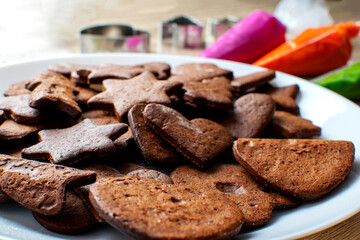 On a wooden table there is a white plate on which gingerbread cookies and icing next to them. Baking concept