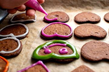 A young chef decorates the gingerbread cookies with pink icing, draws the eyes and mouth. Baking concept