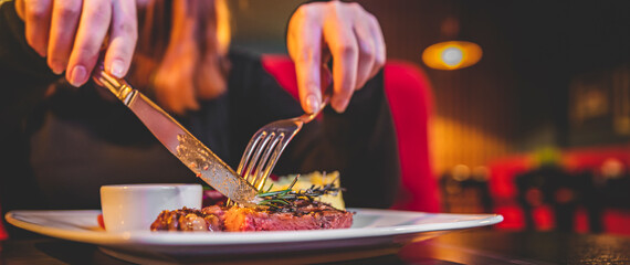 woman hands with fork and knife eating beef steak in cafe