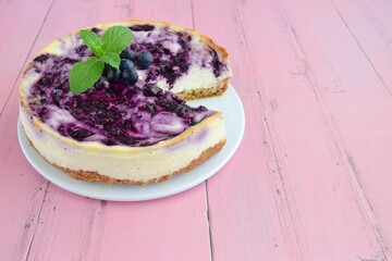 Homemade swirl blueberry cheesecake garnish with fresh blueberries and mint leaf on pink background