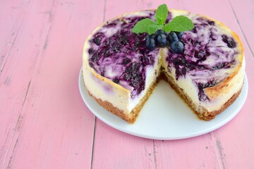 Homemade swirl blueberry cheesecake garnish with fresh blueberries and mint leaf on pink background