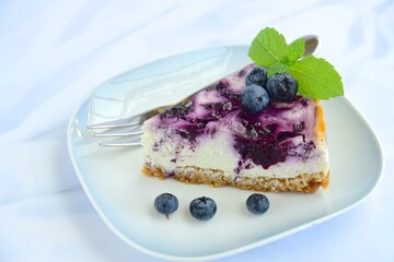 Slice of blueberry cheesecake with mint leaf on white background