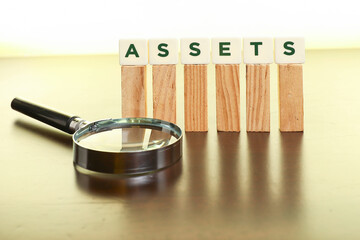 Assets management concept.  Block letters on Assets on the wooden sticks with a magnifying glass on the wooden table 