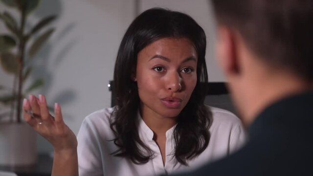 Closeup woman face sit in office chair and talk to colleague during break Spbi. 30s mixed ace female exchanging creative thoughts work ideas with coworker man, hold pen. Concept consult, advisor