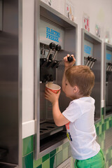 Fototapeta na wymiar A cute kid pours liquid ice cream from a vending machine into a bowl. A cafe with self-service machines.