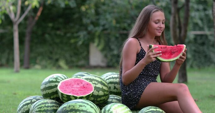 Teen girl sitting in the garden and eating watermelon. Copy space. 4k video.