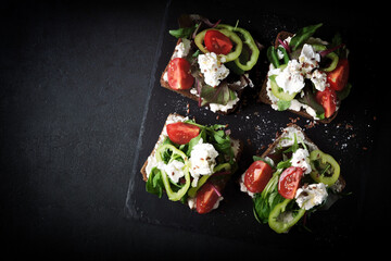 Healthy open sandwiches with salad and white cheese on a black background. The keto diet. Keto snack.