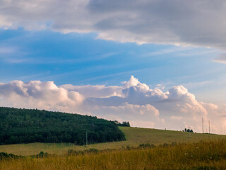 Massive clouds - towering cumulus - forming in the blue sky behind hilly landscape on the horizon