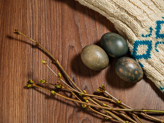 Painted eggs, willow twigs with green kidneys lie on brown surface of rows with knitted jacket