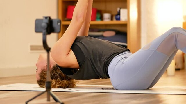 Flexible woman performing supine yoga exercise on mat at home