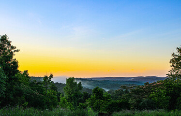 sunset shining over the mountains as fog is beginning to form over the tops of the valleys